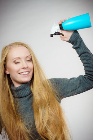 Young female long blonde hair holding bottle, applying hair spray.の写真素材