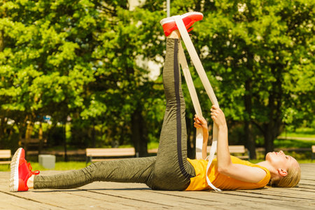 Young woman exercises outdoor in park, using gym accessory fitband. Staying fit and healthy.の写真素材