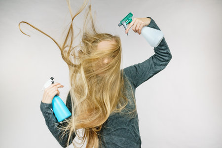 Young female messy long blonde hair holding bottle, applying hair spray.の写真素材