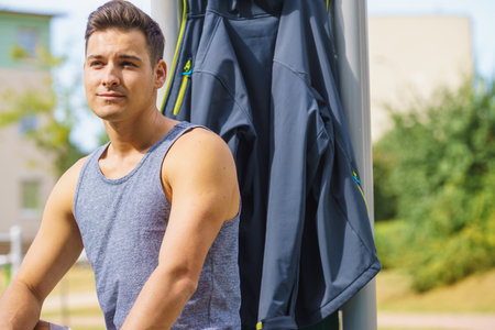 Handsome guy relaxing after outdoor workout. Fit man feeling healthy, enjoying sun. Exercising on public gym equipment in the open air.の写真素材