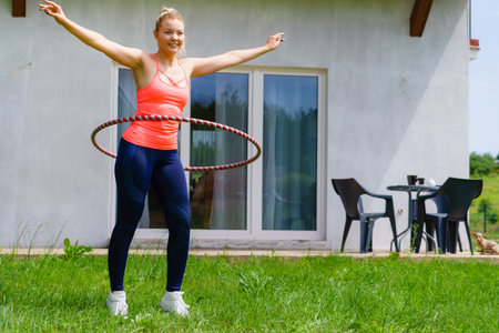 Woman using hoola hoop for slim waist, doing exercises gym outdoor in garden. Workout sport and training.の写真素材
