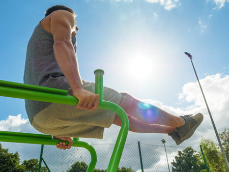 Young man working out in outdoor gym, doing leg lifting abs exercise. Staying fit and healthy.の写真素材