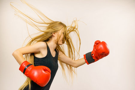 Blonde long hair woman in big red boxing gloves. Female fight for equal rights for women. Side view. Gender equality concept.の写真素材