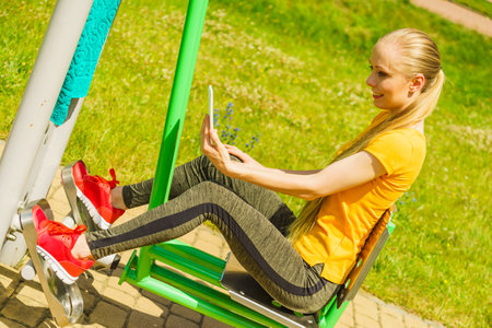 Young woman working out in the outdoor gym. Girl taking selfie photo with smartphone while doing exercises on street machine.の写真素材