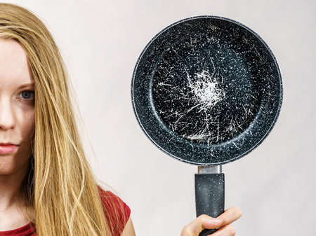 Woman holding scratched frying pan, cause of cancer. Torn coating, kitchen utensils is unusableの写真素材