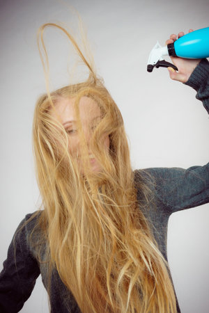 Young female messy long blonde hair holding bottle, applying hair spray.の写真素材