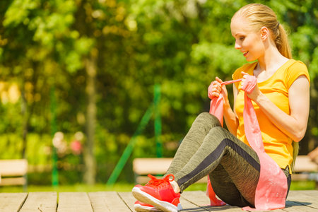 Young woman exercises outdoor in park, using gym accessory, resistance band, strap elastic. Staying fit and healthy.の写真素材