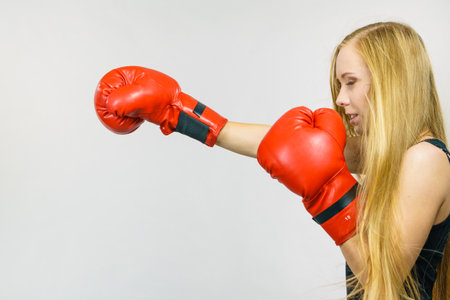 Blonde long hair woman in big red boxing gloves. Female fight for equal rights for women. Side view. Gender equality concept.の写真素材
