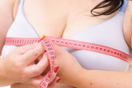 Closeup of female breasts. Plus size fat woman wearing bra using tape measure to check the measurements of her big chest. Bosom, brafitting and underwear concept.の写真素材