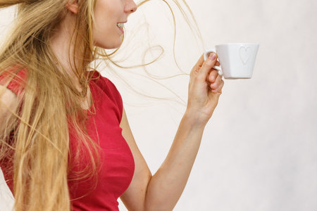 Blonde girl with blowing long hair holds heart shaped coffee cup, on greyの写真素材