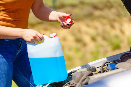 Woman pouring blue antifreeze liquid for car windshield screen washing with bootle watering canの写真素材