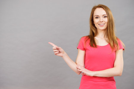 Woman pointing with finger at copy space with surprised face expression, on greyの写真素材