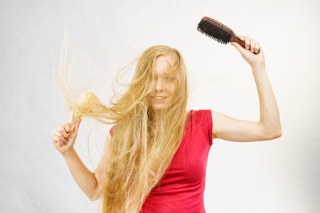 Blonde girl long blowing hair holds two brushes, one with natural bristles. Haircare, treatment concept.の写真素材