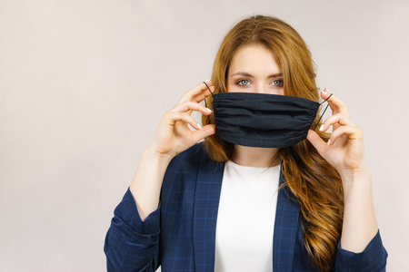 Woman using black protective reusable face mask, covering mouth. Coronavirus prevention. Health and safety.の写真素材
