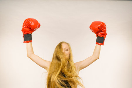 Blonde long hair woman wearing big red gloves standing with arms up, celebrating success. Female...
