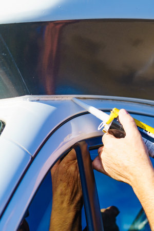 Person hand applying silicone sealant around the edges of caravan. Man inspect and replace camper car seals.の写真素材