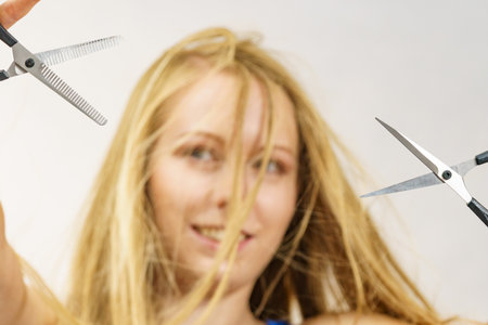 Haircut coiffure haircare concept. Girl with blowing long blond hair holding scissors, showing work tools, normal and thinning shears.の写真素材