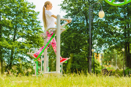 Full body of woman working out in outdoor gym. Girl doing legs exercises on street public equipment on sunny dayの写真素材