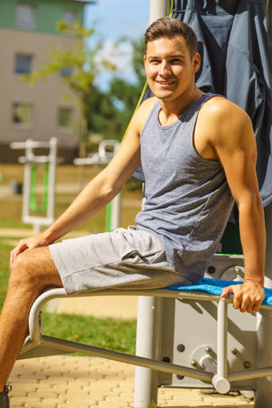 Handsome guy relaxing after outdoor workout. Fit man feeling healthy, enjoying sun. Exercising on public gym equipment in the open air.の写真素材