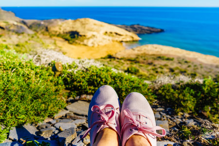 Female feet in sneakers against mediterranean sea coast landscape. Murcia region, Calblanque Park in Spain. Hiking, vacation activity.の写真素材