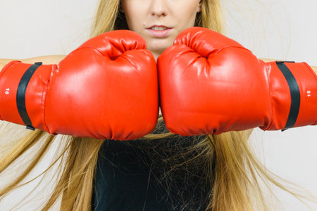 Blonde long hair young woman in big red gloves boxing, playing sports. Female fight for equal rights...