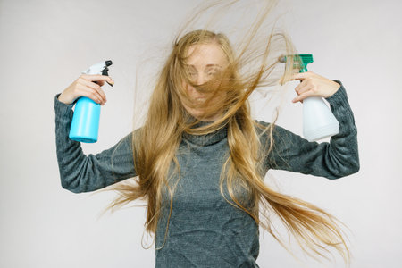 Young female messy long blonde hair holding bottle, applying hair spray.の写真素材