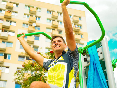 Young handsome man working out in outdoor gym. Sporty guy flexing his muscles on machine. Staying...