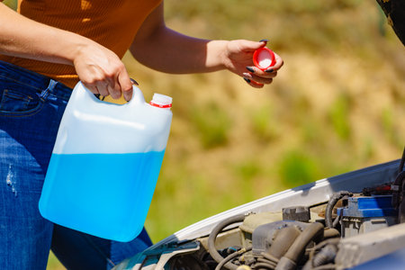 Woman pouring blue antifreeze liquid for car windshield screen washing with bootle watering canの写真素材