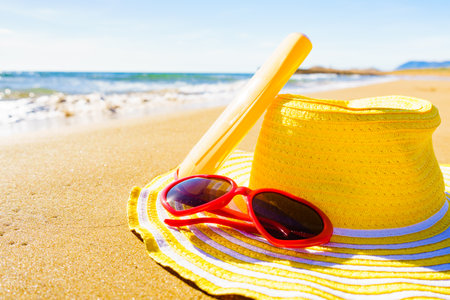 Sun protection accessories on sea shore. Red sunglasses, yellow straw hat and sunscreen cream bottle...