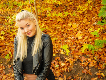 Blonde woman wearing fashionable outfit. Happy female in black leather jacket walking in autumnal...