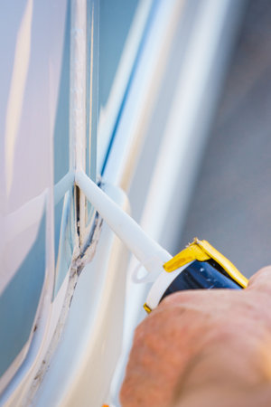 Person hand applying silicone sealant around the edges of caravan. Man inspect and replace camper car seals.の写真素材