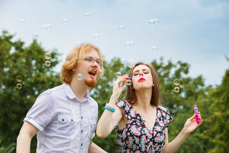 Happiness and carefree concept. Young woman and man having fun blowing soap bubbles together on...