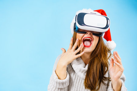 Woman wearing santa claus hat exploring space with virtual reality goggles headset. Emotional female...