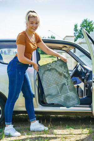 Woman cleaning car interior, holding dirty rubber car floor matの写真素材
