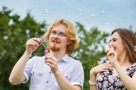 Happiness and carefree concept. Young woman and man having fun blowing soap bubbles together on...