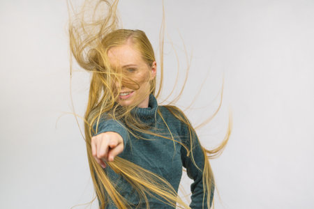 Smiling girl with blowing long blonde hair pointing with finger at you.の写真素材