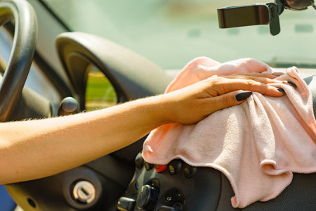 Hand cleaning car dashboard with cloth.