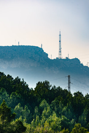 Telecommunications tower mast and power lines, high voltage electricity transmission pylons in mountains.の写真素材