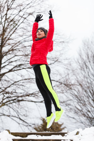 Outdoor sport exercises, sporty outfit ideas. Woman wearing warm sportswear training exercising outside during winter jumping out of joyの写真素材