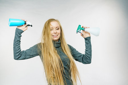Young female messy long blonde hair holding bottle, applying hair spray.の写真素材