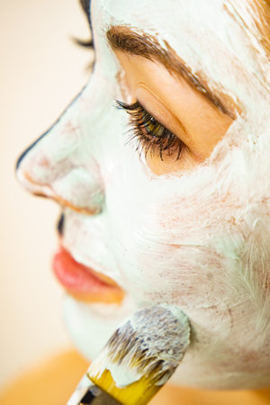 skincare. Female applying green purifying mud mask, cosmetic healing clay to face, using brush. Beauty and wellness. Spa and acne treatment.の写真素材