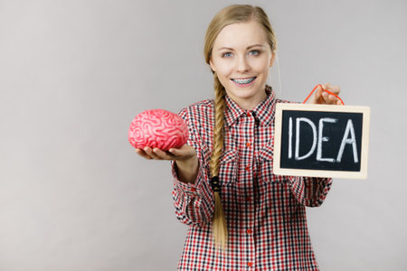 Young woman holding idea sign banner on black board and fake brain. Studio shot on grey.の写真素材