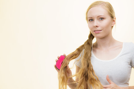 Blonde girl with brush combing her long hair. Girl taking care refreshing her hairstyle. Haircare concept.の写真素材