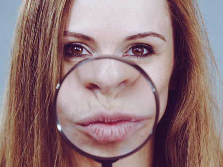 Happy young woman showing big lips through magnifying glass. Lip enlargement concept.の写真素材