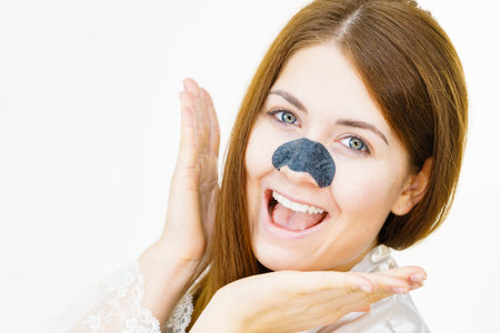 Woman applying clear-up strips on nose, using pore cleansing textile mask for blackheads. Girl taking care of skin complexion. Beauty treatment. Skincare.の写真素材