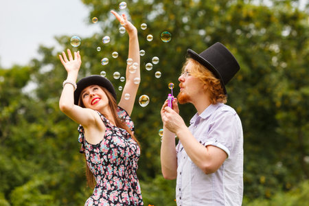Happiness and carefree concept. Young woman and man having fun blowing soap bubbles together on nature.の写真素材