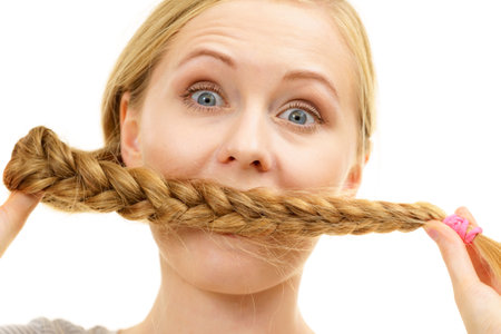 Blonde girl covering her mouth with long braid hair. Haircare, hairstyling.の写真素材