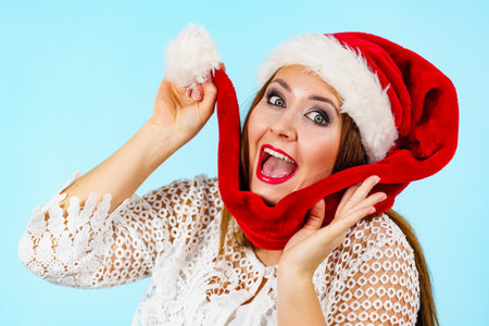 Happy excited young woman wearing santa claus red hat, on blue. Christmas holiday season.の写真素材
