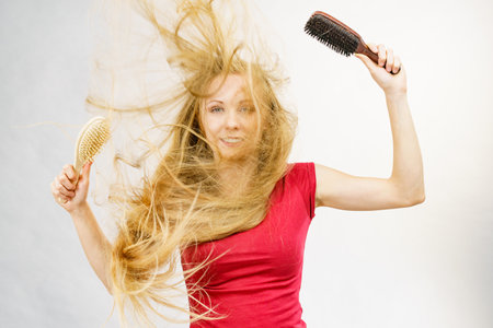 Blonde girl long blowing hair holds two brushes, one with natural bristles. Haircare, treatment concept.の写真素材