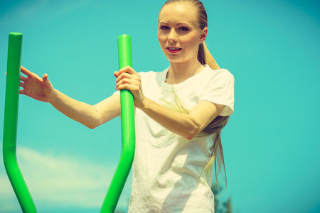 Young woman doing exercises on public equipment in city park. Girl working out training in outdoor gym. Healthy lifestyle.の写真素材